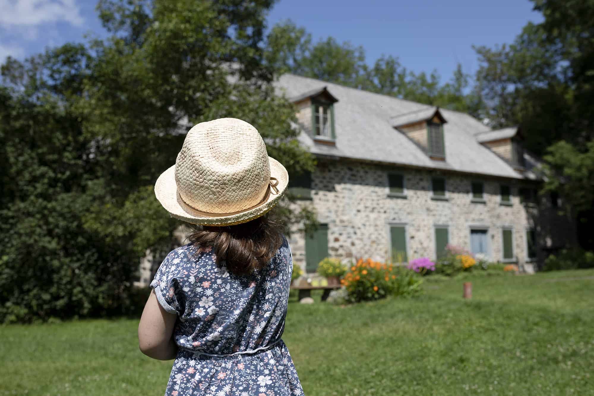 Enfant regardant une maison en pierre et jardin.