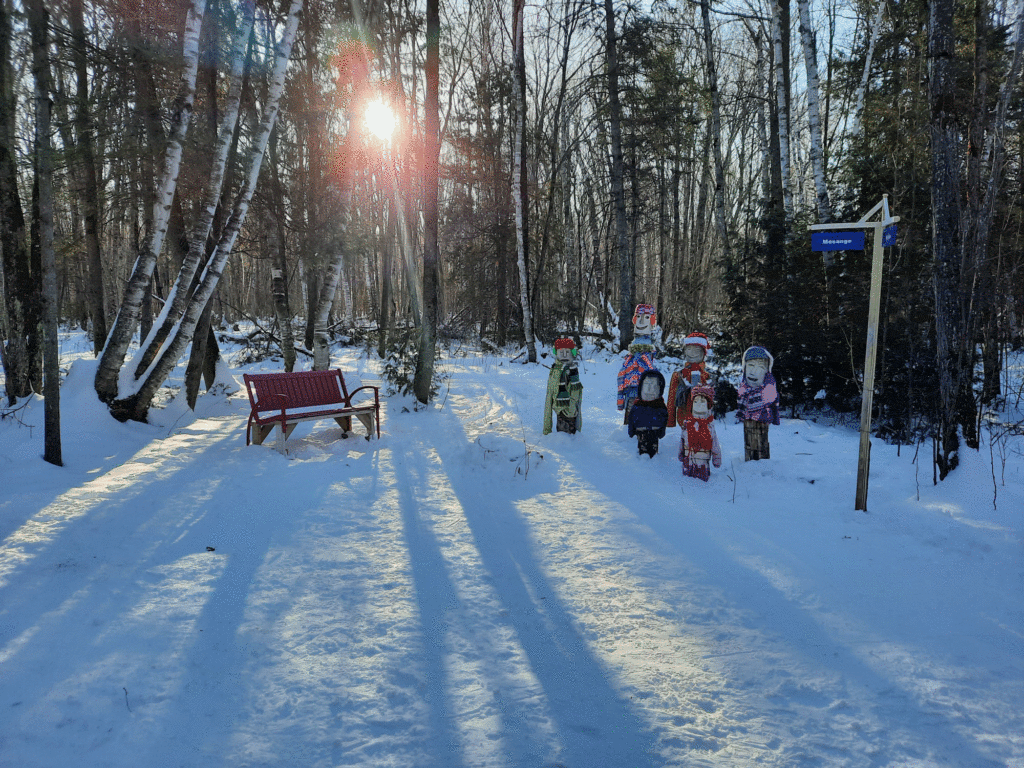 Banc rouge et sculptures dans forêt enneigée.