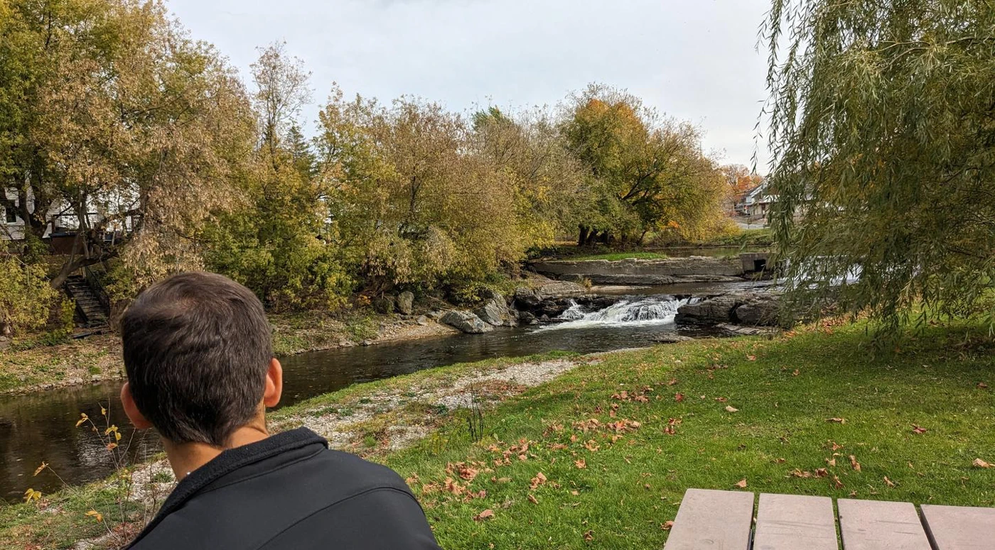 Homme contemplant rivière et arbres en automne.