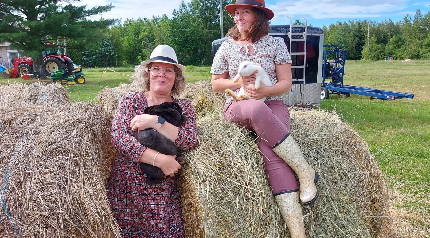 Deux femmes tenant des lapins dans une prairie.