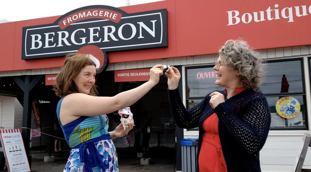 Deux femmes dégustent du fromage devant fromagerie.