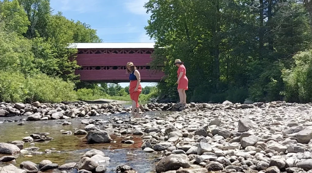 Pont couvert rouge avec deux personnes près d'une rivière.