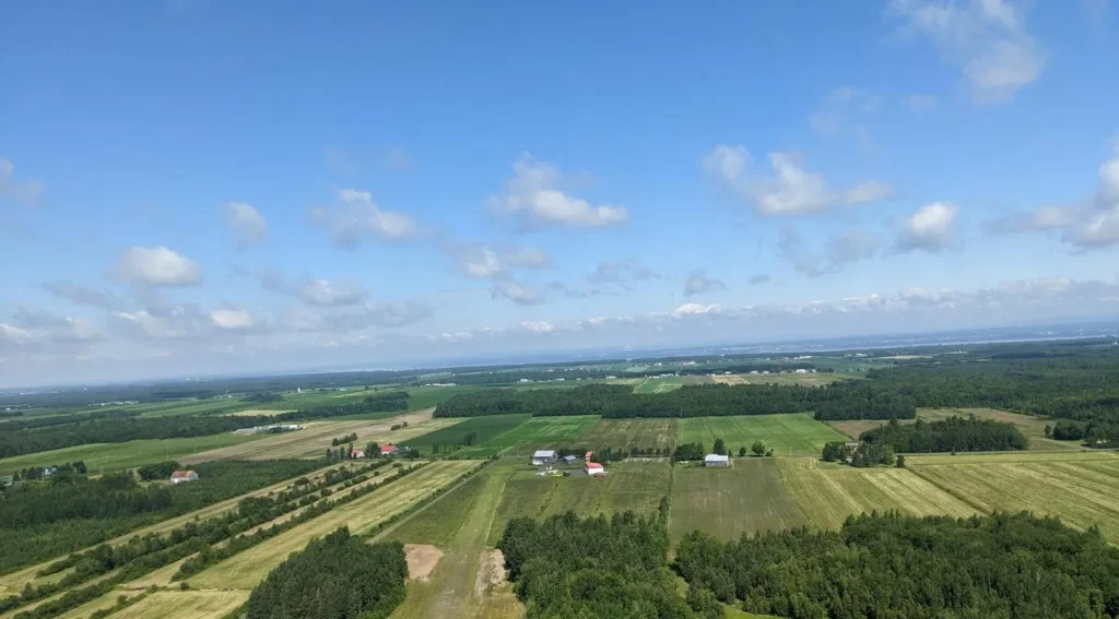 Vue aérienne de paysages agricoles verdoyants sous ciel bleu.