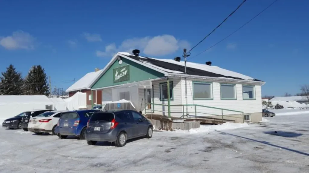 Bâtiment enneigé avec voitures garées devant.