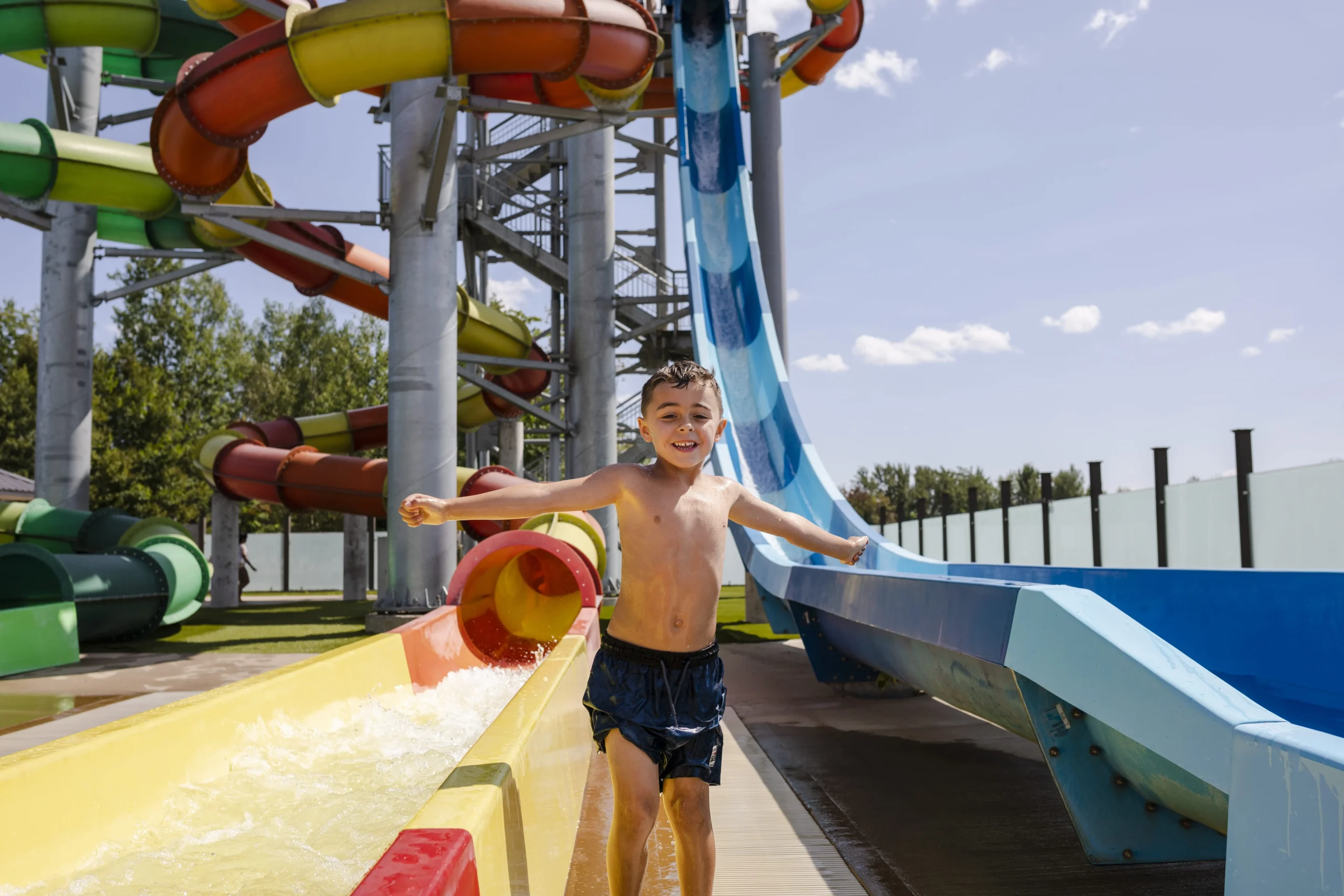 Enfant souriant devant des toboggans aquatiques colorés.