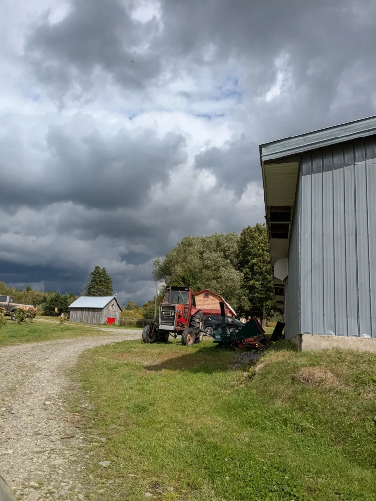 Tracteur rouge près d'un bâtiment gris, ciel nuageux.
