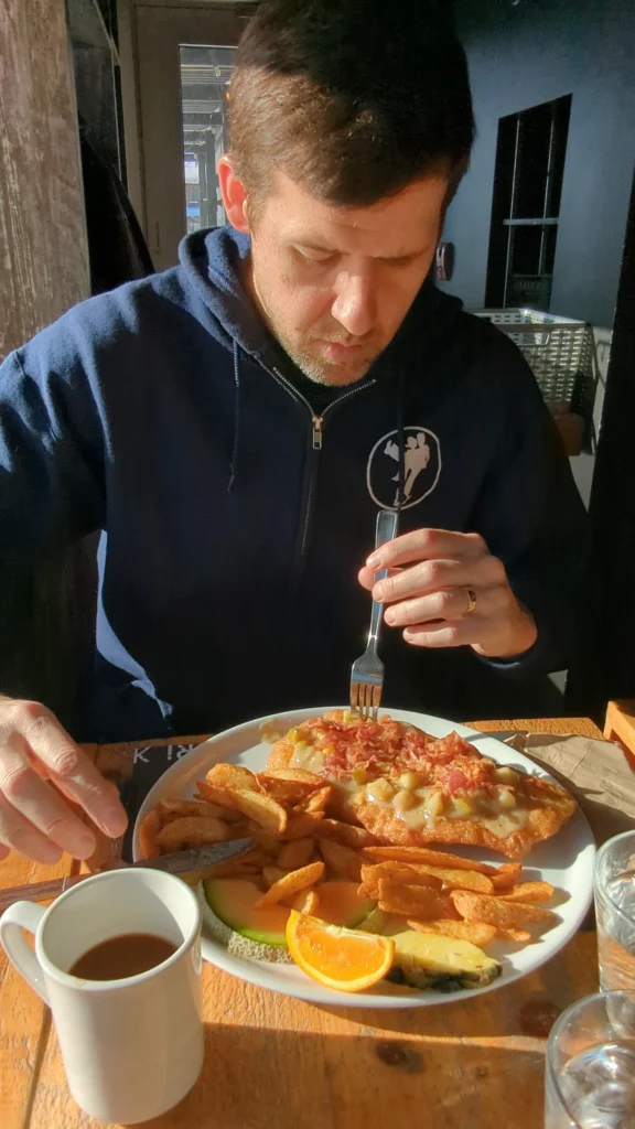 Homme mangeant plat avec café et fruits.
